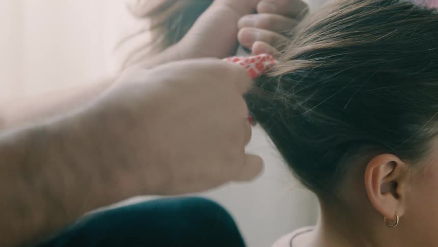 A father puts a hair tie on his daughter