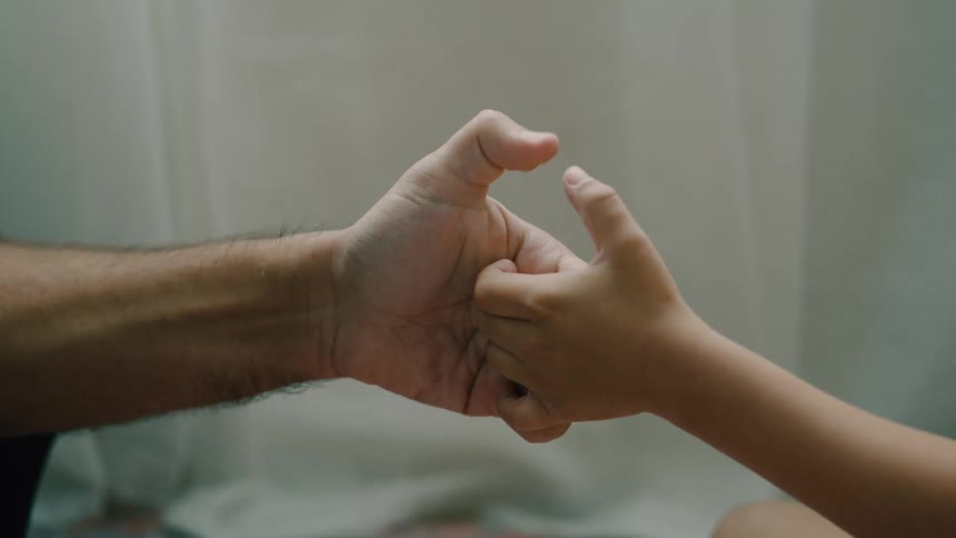 Close up father and sons hands thumb wrestling while sitting on the carpet