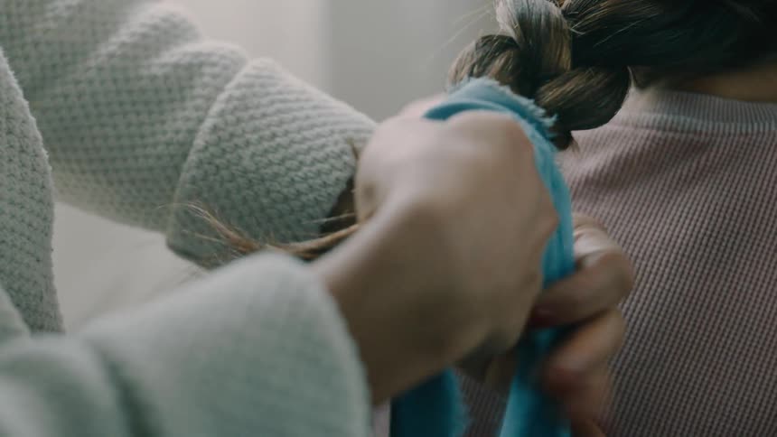 A mother is braiding and tying her daughters hair