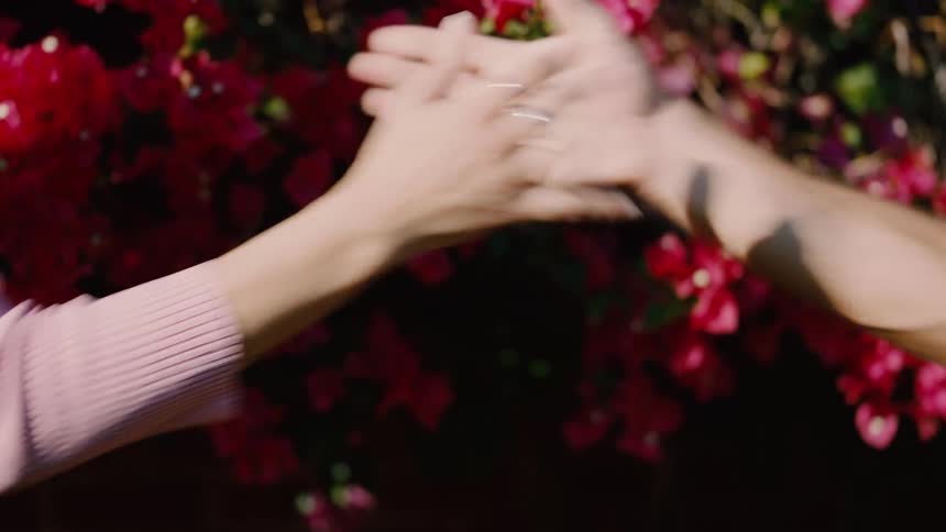 Man and woman perform a complicated handshake while standing near a large flowering bush