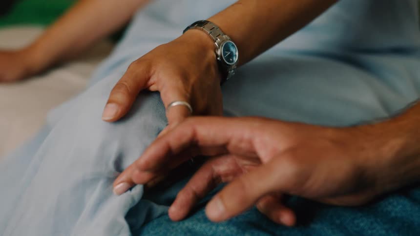 Close up of a couples hands and they gently touch each others fingers while sitting