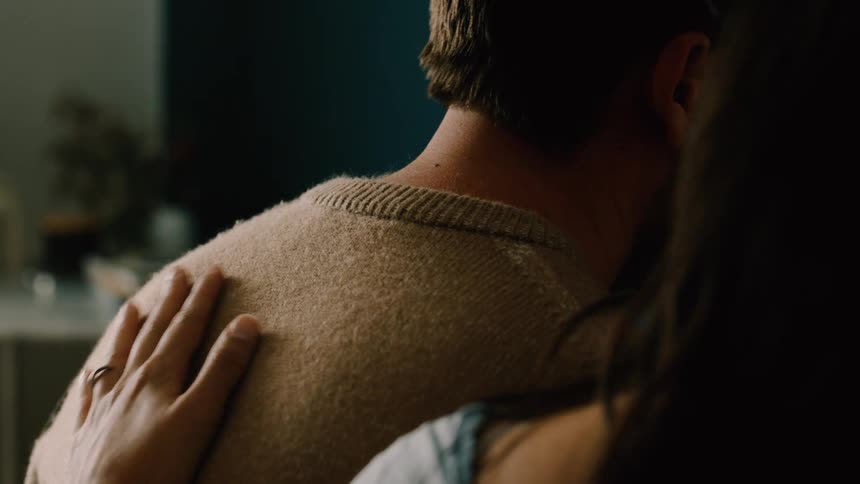A woman gently touches a mans back in a caring moment