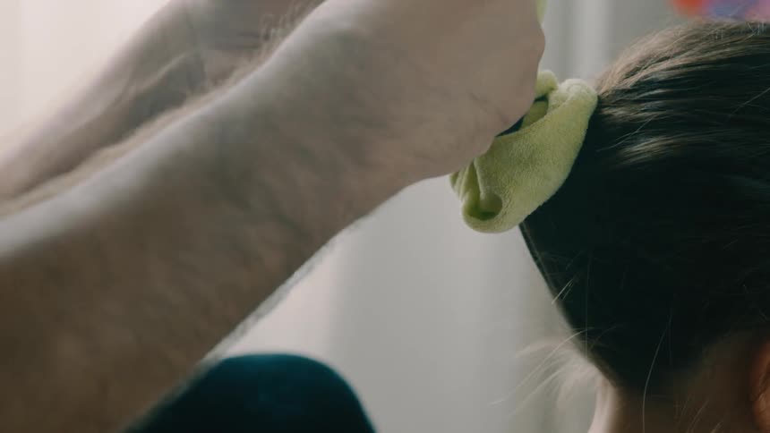 A father is putting a hair tie on his daughter