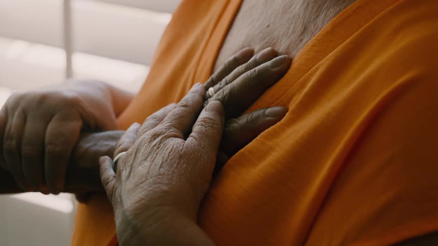 An elderly person places both hands over their chest in a gesture of emotion or reassurance