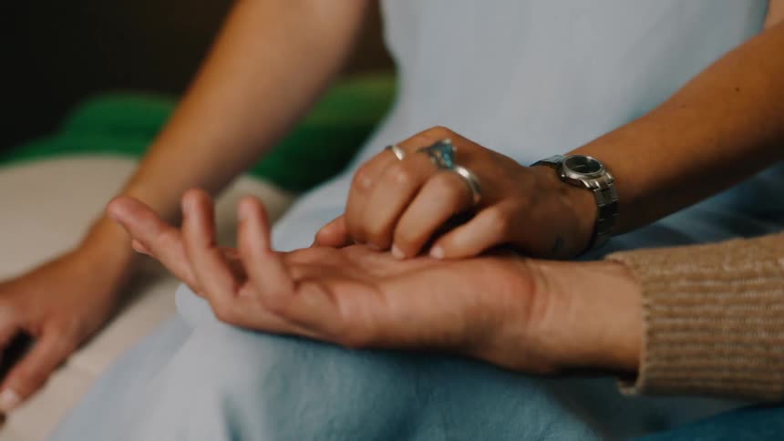 A couple sits closely together holding hands affectionately as the woman displays rings on her fingers and a wristwatch on her wrist