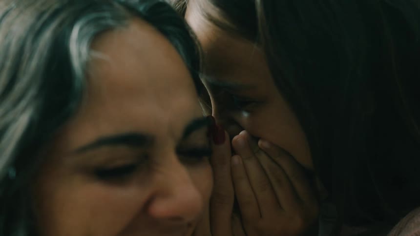 Girl child playfully whispers into a womans ear in a room