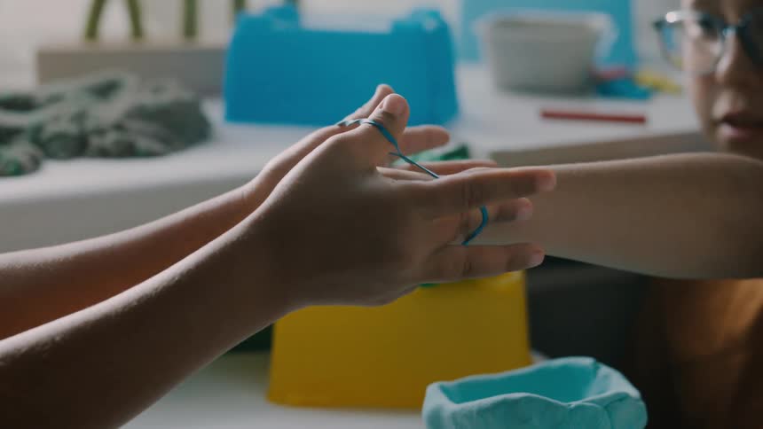 Children are playing a fingerstring game together at a crafting table