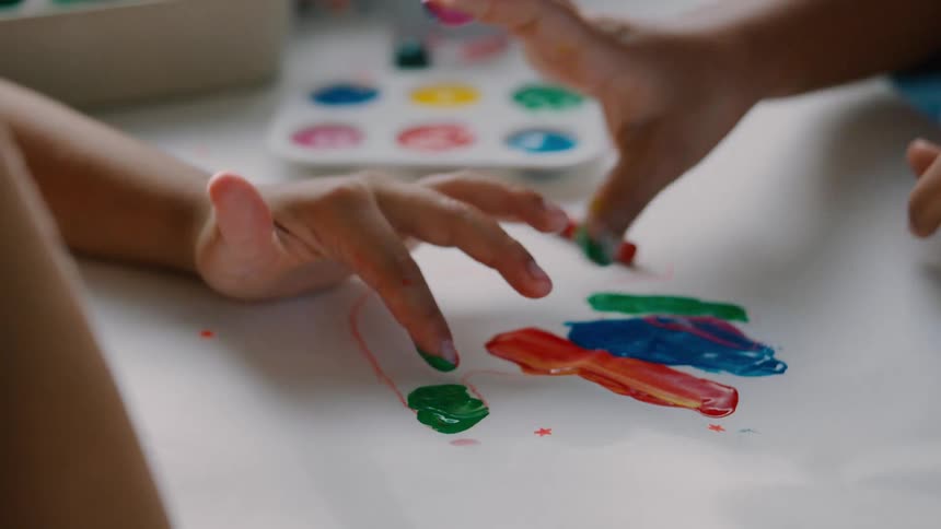 Close up of kids hands finger painting with bright colors on white paper
