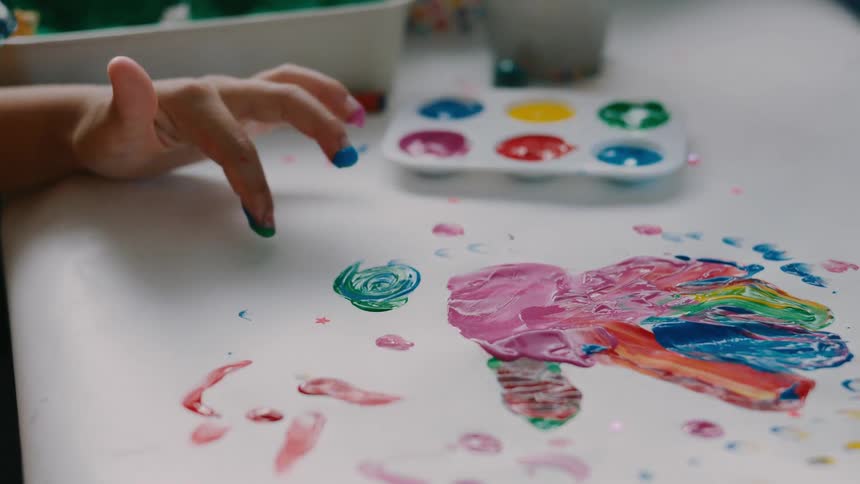 Close up of two children making an abstract painting with water colour by using their fingertips