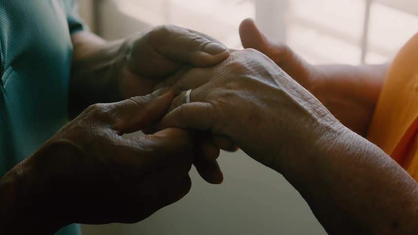 An elderly couple holding hands as the man adjusts a ring on the womans finger