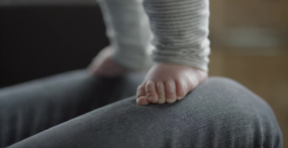 A baby standing on a person's legs