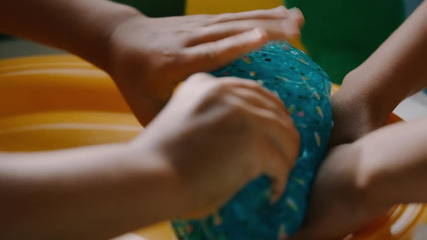 Childrens hands are squishing a blue slime toy in a yellow tray during playtime
