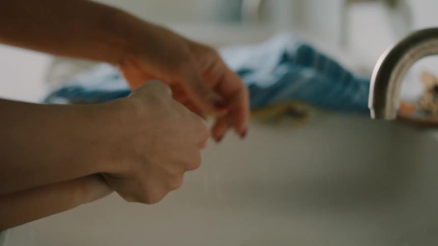 The hands of an adult holding the hands of a child to wash in a sink and then dry with the blue cloth