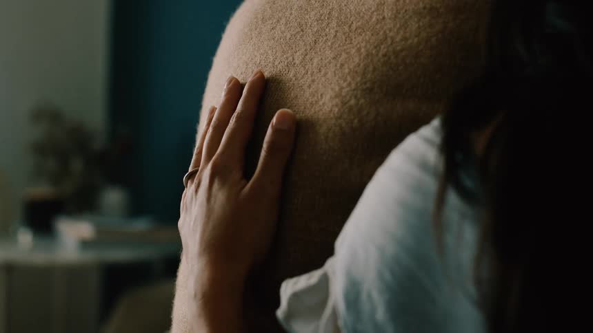 Close up of a womans hand as she rubs the back of her male partner seated in a room