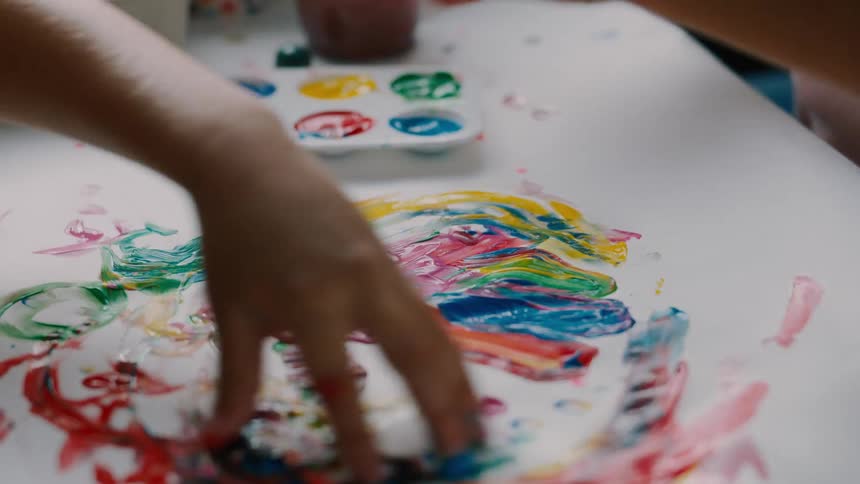 Two kids finger painting with colorful paint on white paper