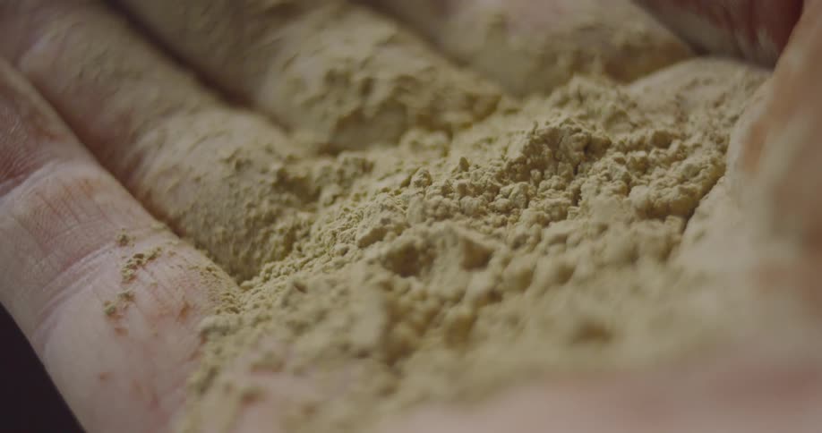 A man holds a beige powder in his hand