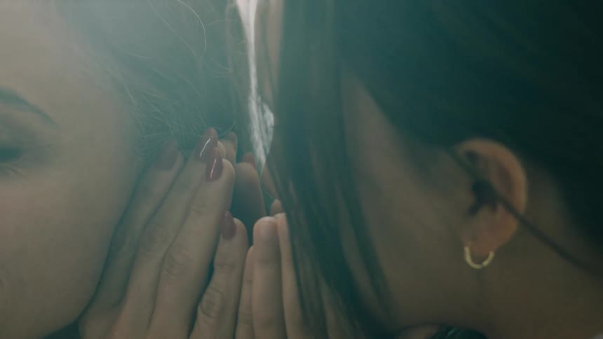 A child whispers a secret into her mothers ear both laughing joyfully
