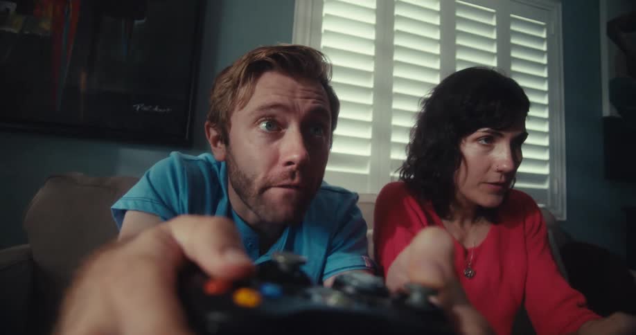 Man and woman compete and celebrate while playing video games with controllers on a couch in a living room