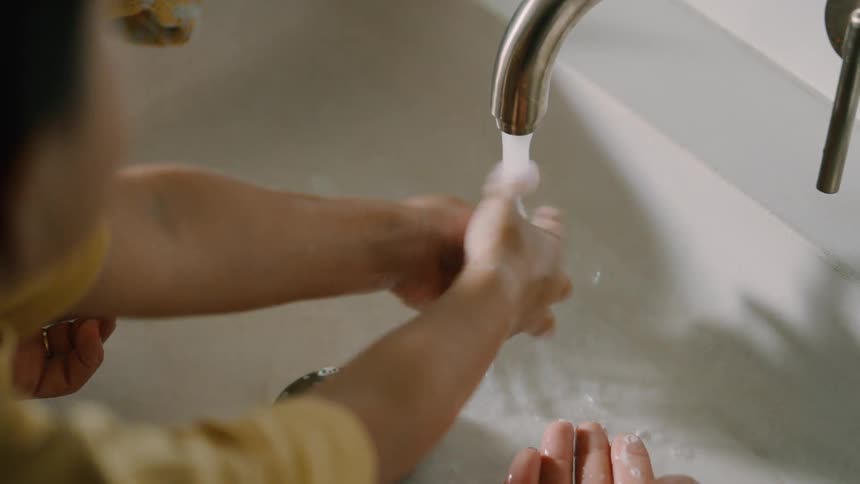 A boy washes his hands in a sink while an adult assists him