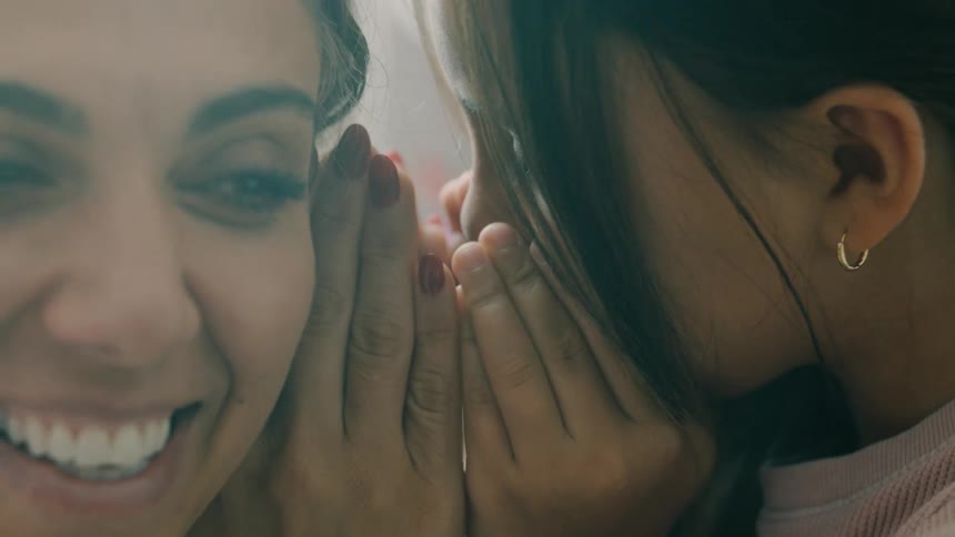 A little girl whispers into her mothers ear and laughs playfully