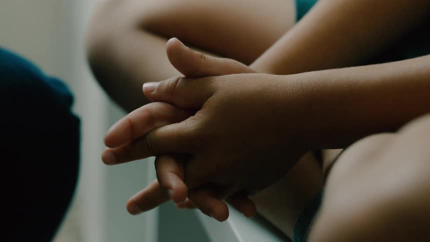 Mother comforts her child when the kid nervously interlaces their own hands