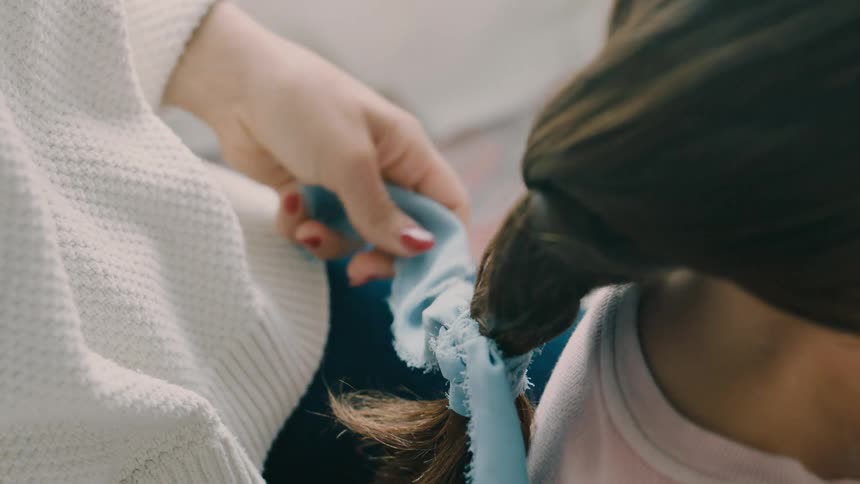 Mother gently tying a braid with a ribbon in a young girls hair