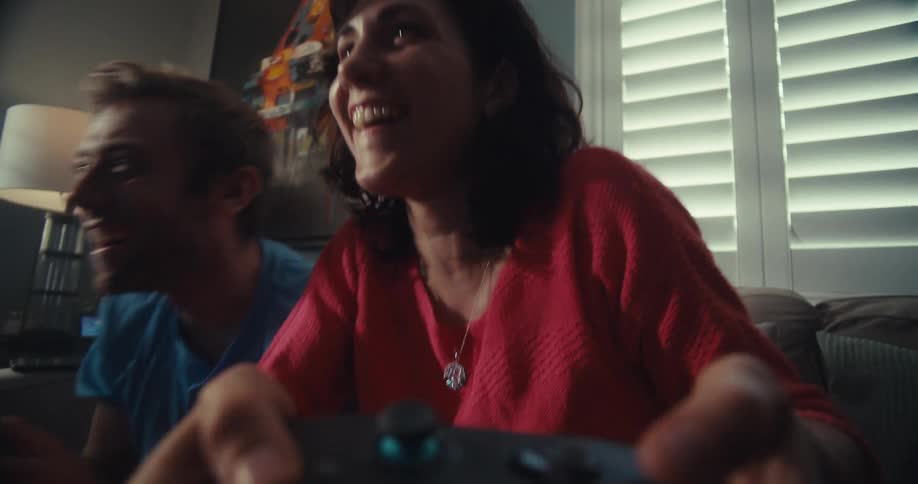 Man and woman happily compete while playing video games on a couch in a living room