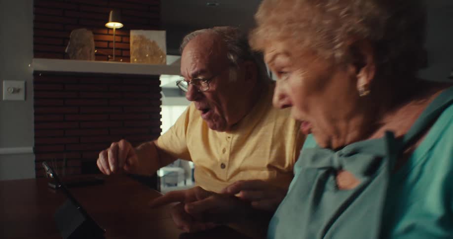 A happy couple looks shocked and excited while reacting to something on a tablet