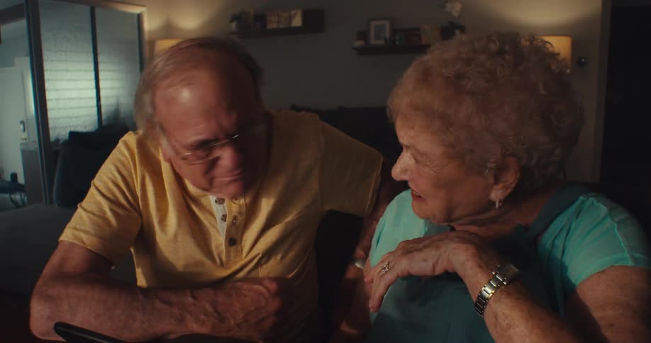 A happy elderly couple laughs while chatting and looking at a tablet together
