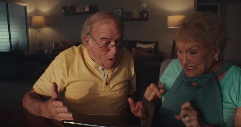 A man and woman talk while watching a tablet