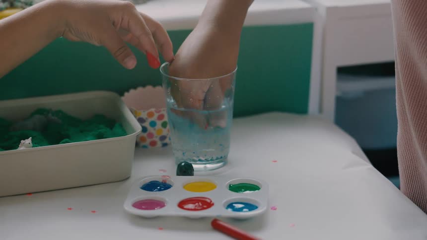 Two kids are rinsing paint off their fingers in a glass of water