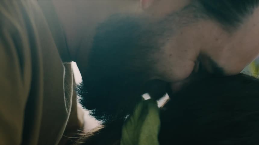 Man rests on and kisses a females hair while smiling in a room