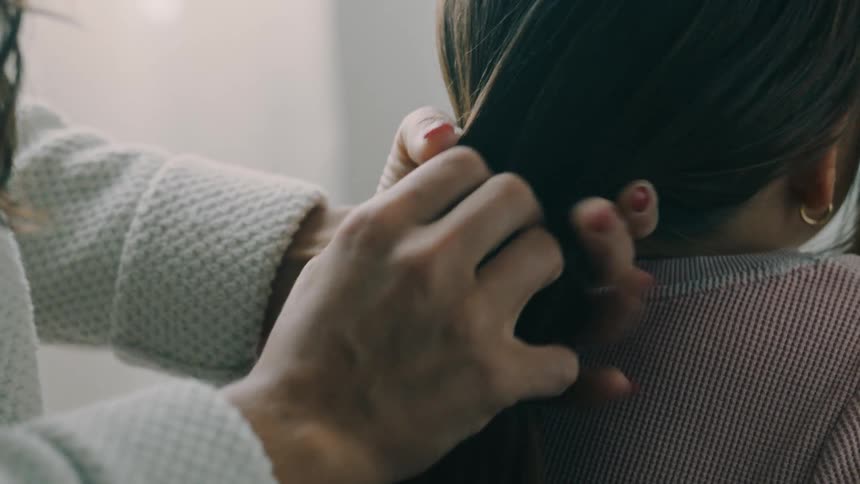 Close up of a woman arranging a childs hair into a ponytail