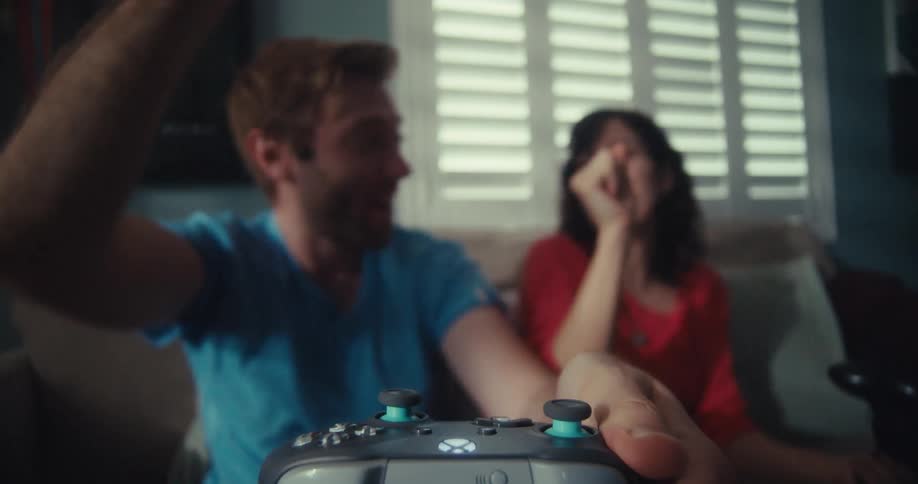 A couple sits on a couch playing a video game with great excitement at midday