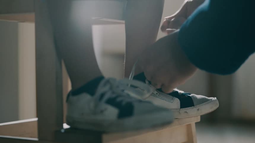 A person lacing the shoe of someone seated on a wooden chair