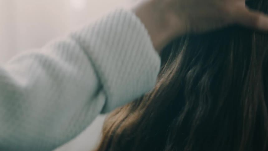 Woman strokes the hair of another female while they are indoors during the daytime