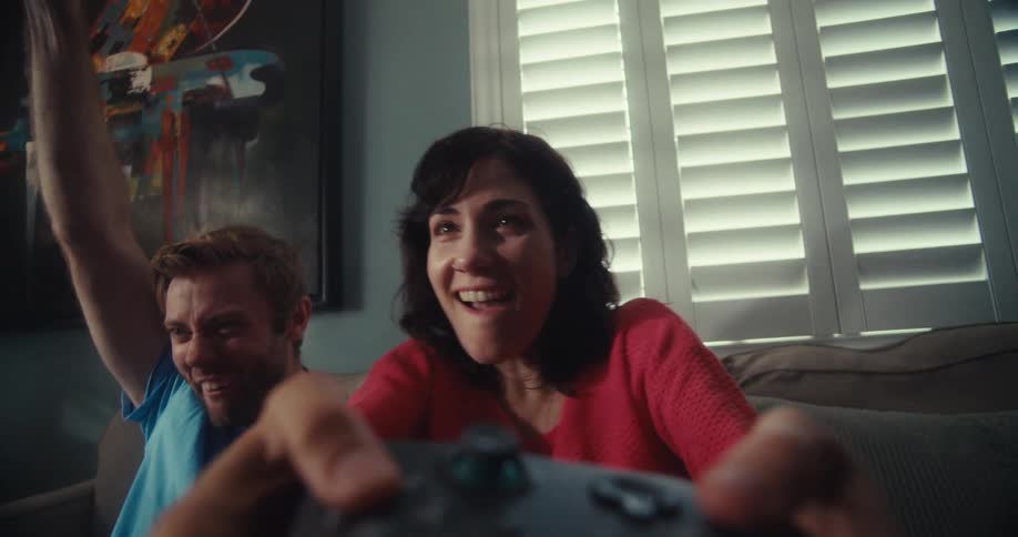 A young couple plays video games together the woman holding the controller as the man celebrates in the room