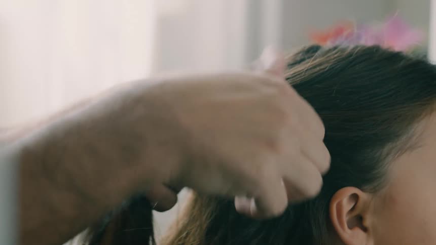 The hands of an adult person arranging the hair of a little girl who is sitting looking forward