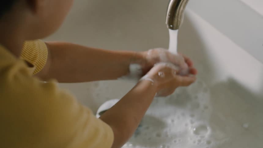 Boy rinses his hands of soap lather in a white porcelain bathroom sink