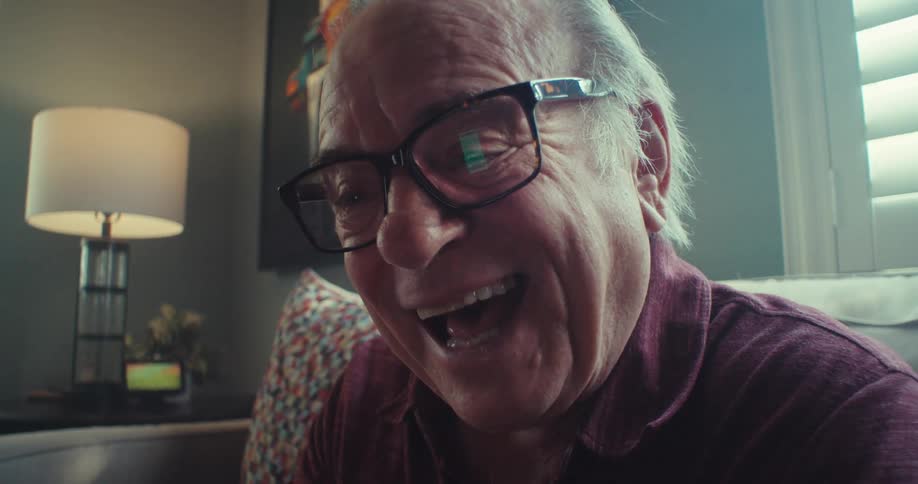 An older man wearing glasses is smiling while talking on a video call at home