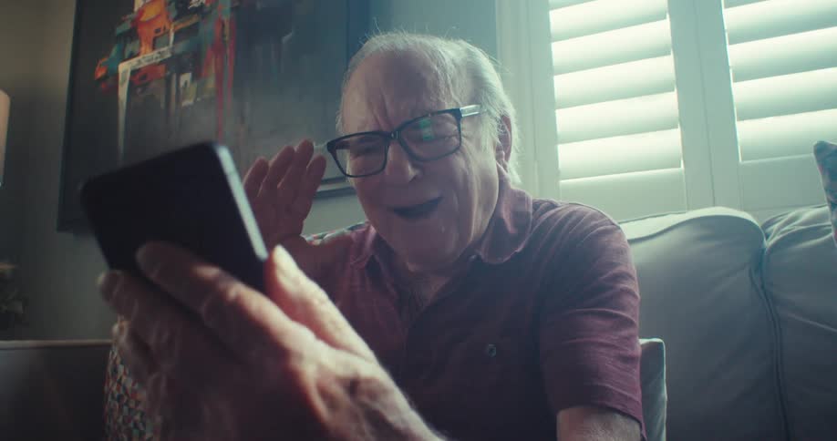 Happy elderly man sitting on a sofa and interacting with a smartphone