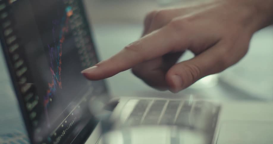 A persons finger points to a financial data graph on a laptop screen analyzing trends