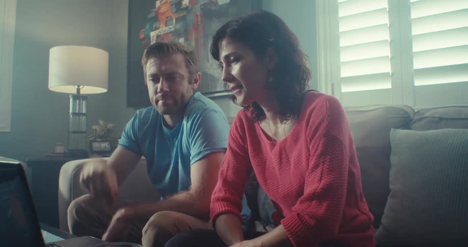 Two people sitting on the couch talking and pointing at a laptop screen