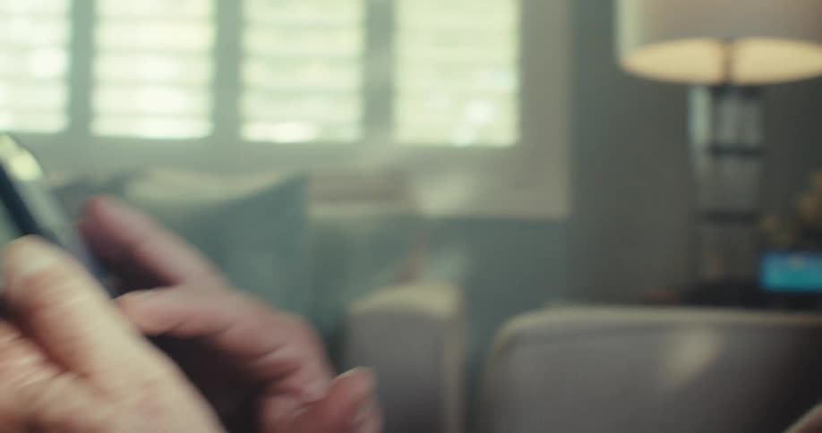 An elderly man indoors looks worried while using a smartphone