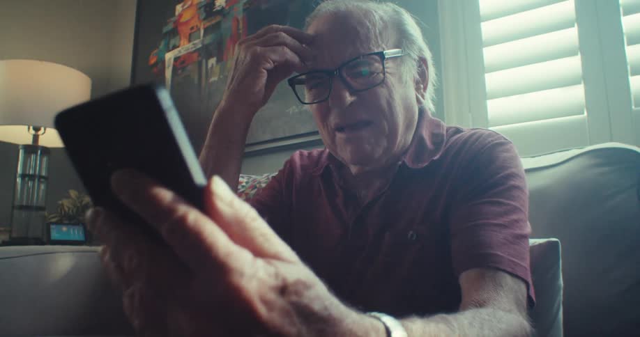 An elderly man on a sofa speaking aggressively on the phone