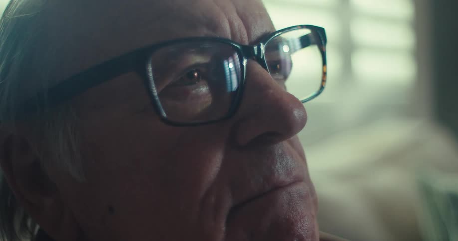 An elderly man sitting on a sofa looking straight ahead deep in thought