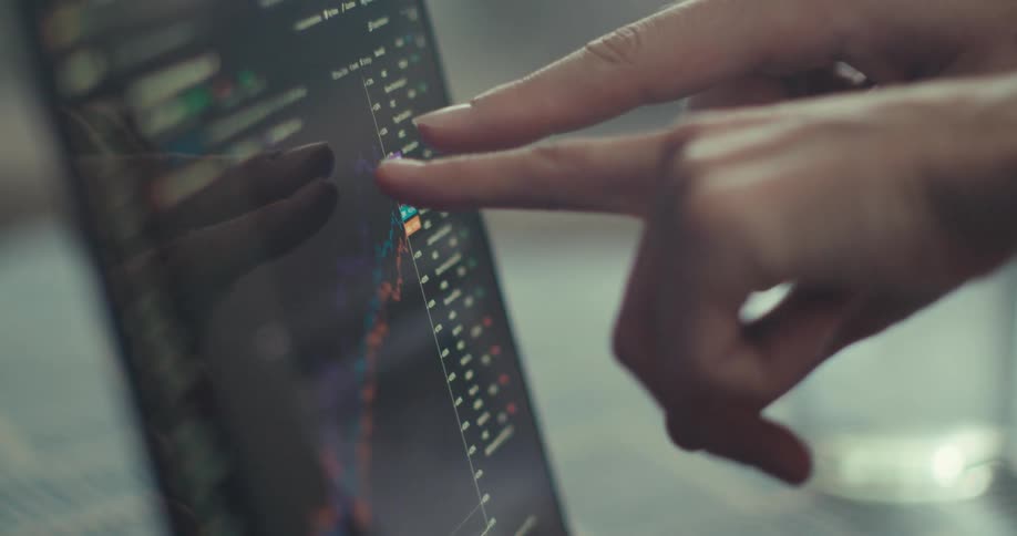 Hands of two people pointing at a laptop screen displaying a graph