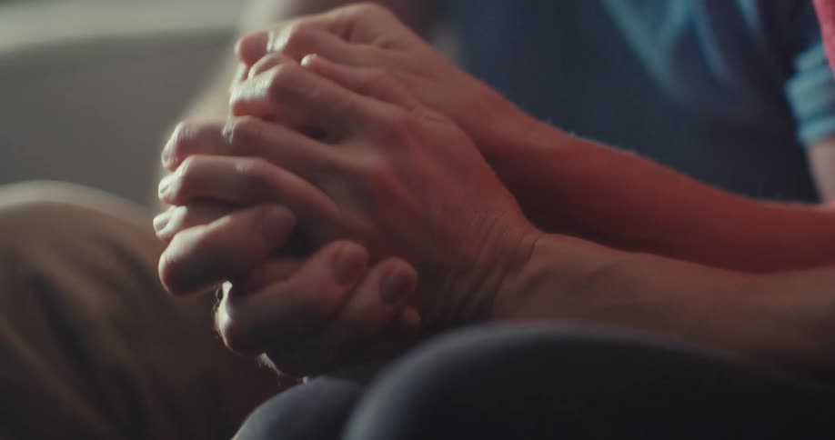 A couple sits indoors holding hands sharing a warm and loving moment
