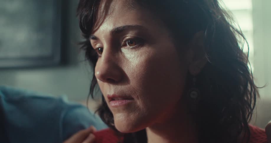 A woman gazes off to the side with a serious expression as a man holds her shoulders in a consoling gesture