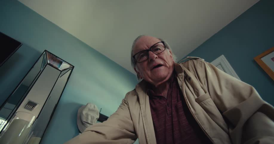 An elderly man walking with the help of a walker entering the house and closing the door